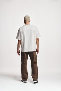 Maglietta di cotone beige chiaro a maniche corte, abbinata a pantaloni cargo marroni larghi con tasche laterali e una trama di stoffa naturale.