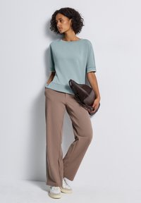 Haut bleu clair à manches courtes associé à un pantalon large beige. La tenue présente une coupe décontractée, avec un sac à main marron texturé comme accent.