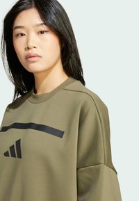 Olivovo zelená mikina s okrúhlym výstrihom, s čiernym vodorovným pruhom a logom troch pruhov, vyrobená z textúrovanej látky.
