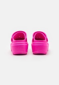 Sabots roses à enfiler avec un extérieur texturé, une sangle au talon et des perforations pour la respirabilité. Nom de la marque embossé sur le talon.