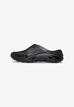Sabots noirs avec un design texturé et ondulé. Fabriqués en matériau léger, dotés de trous de ventilation et d'une forme contournée pour le confort.