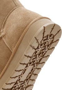 Jasnobrązowe zamszowe buty z teksturowaną cholewką, gumową podeszwą z wzorem śnieżynki i wzmocnionymi krawędziami. Design skupiony na trwałości i przyczepności.