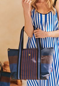 Striped tote bag in blue and brown, featuring dual-color fabric with varying stripe patterns. Includes sturdy handles and a zip closure.