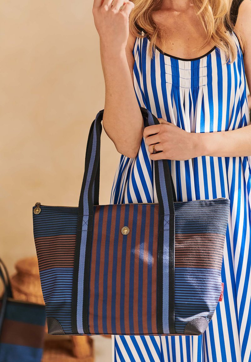 Striped tote bag in blue and brown, featuring dual-color fabric with varying stripe patterns. Includes sturdy handles and a zip closure.