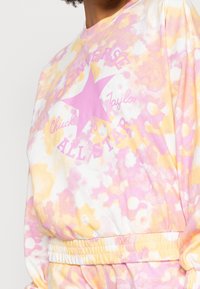 Sweatshirt en coton avec un motif tie-dye pastel rose et jaune, orné d'une grande étoile rose et du texte « Converse All Star » imprimé sur le devant.