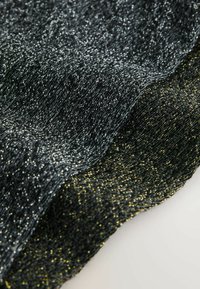 Černá a zlatá metalická pletenina s texturovaným povrchem, která má jemný lesk a vlnitý okraj. Měkký, flexibilní materiál.