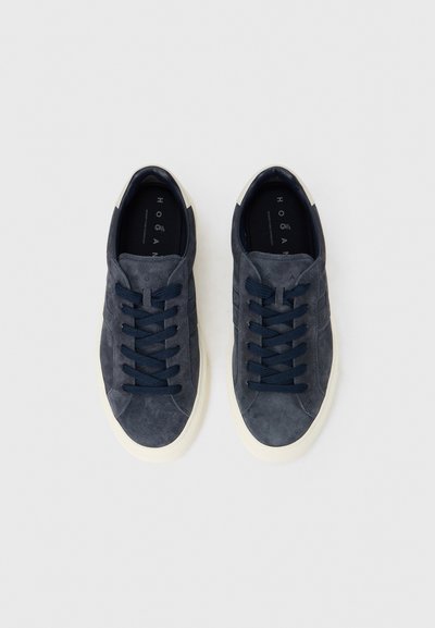 Μπλε σουέντ αθλητικά παπούτσια με κρεμ σόλες από καουτσούκ. Διαθέτουν κορδόνια σε αντίθετο χρώμα και ραμμένες λεπτομέρειες. Χωρίς εμφανές λογότυπο στην εξωτερική πλευρά.