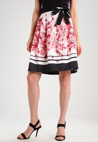 Jupe à imprimé floral avec une base blanche, présentant des motifs de fleurs roses, une taille noire et un ourlet foncé avec des rayures. Accent en noeud noir.