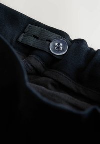 Ceinture en tissu noir avec un bouton transparent et une sangle tissée pour le réglage. Texture lisse avec plusieurs couches de tissu visibles.