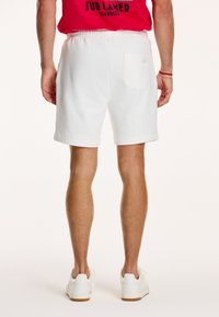 Pantaloni scurți albi din bumbac cu talie elastică, având un buzunar posterior și o croială lejeră. Purtați cu adidași albi.