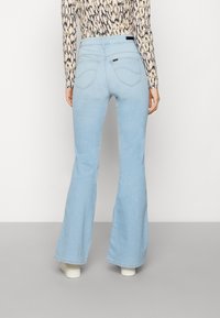 Light blue flared jeans in denim with a mid-rise waist, featuring back pockets and subtle stitching details. Worn with a patterned top.