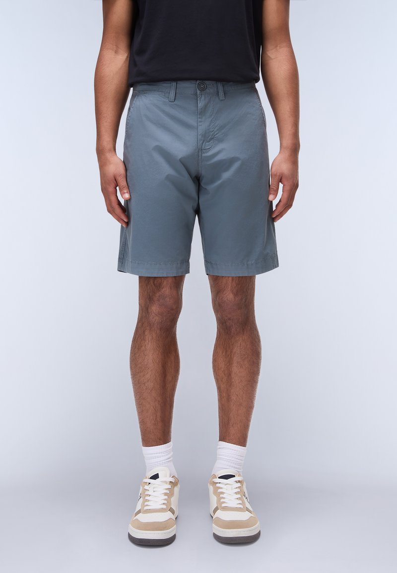 Grå shorts i lättviktsmaterial, med knappstängning, sidofickor och fållade fållar. Kombinerat med beige sneakers och vita strumpor.