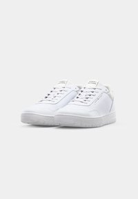 Baskets blanches en matériau synthétique, présentant une texture lisse, un bout arrondi, une semelle plate en caoutchouc et un système de laçage avec des accents de marque.