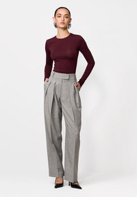 Šedé kalhoty ve stylu Marlene s plisováním, spojené s přiléhavým vínovým topem s dlouhým rukávem a černými lodičkami se špičatou špičkou. Hladká textura, těsně přiléhající design.