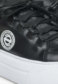 Czarne skórzane sneakersy o teksturowanej powierzchni, płaskich czarnych sznurowadłach i okrągłym białym logo z boku. Posiadają białą gumową podeszwę z wzorowanym gripem.