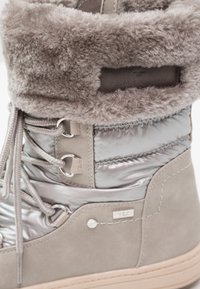 Stivale invernale grigio foderato in pelliccia sintetica, con parte superiore in tessuto argentato lucido, occhielli metallici e suola in gomma texturizzata.