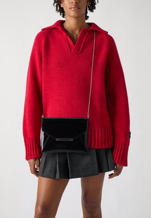 Maglione rosso lavorato a maglia con un colletto, polsini a coste e una borsa a tracolla in vernice nera con un design a patta geometrica.