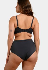 Bralette en dentelle noire avec des bretelles réglables, associée à des culottes taille haute noires. Texture lisse, détails en dentelle délicats sur le soutien-gorge.
