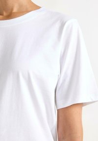 Hvid bomulds T-shirt med en klassisk crew neck, korte ærmer og en glat tekstur. Ingen mærkbare mønstre eller accenter synlige.