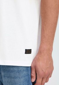 White short-sleeve t-shirt featuring a textured fabric. Includes a black and gold label with "SOLID Denmark Since 1999" stitched on the hem.