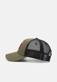 Olivgrön keps med böjd skärm, svart meshbakgrund och röd logotypdetalj framtill. Har sömnadsdetaljer på skärmen.