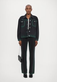 Veste en denim noire avec des accents verts, boutons en argent et poches sur la poitrine, associée à un pantalon assorti. Les accessoires comprennent un petit sac à main noir.