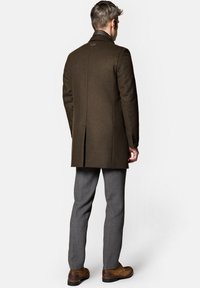 Brązowy wełniany płaszcz o dopasowanym kroju, z rozcięciem z tyłu i klapami, w zestawie z szarymi spodniami i brązowymi skórzanymi botkami.