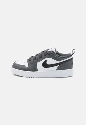 Baskets basses blanches et gris foncé avec un swoosh noir de Nike, fermeture à lacets et semelle en caoutchouc blanche sur fond clair neutre.
