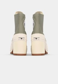 Botas de tobillo de lona verde con suelas de plataforma blancas, que cuentan con parches de logo negro redondeados y costuras en contraste en la parte superior.