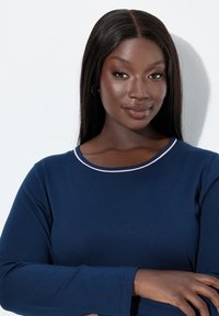 Top a maniche lunghe blu navy con scollo rotondo decorato da un bordo rosa chiaro. Il tessuto sembra liscio ed elastico, con una silhouette aderente.