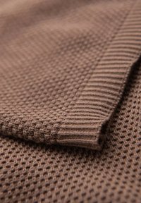Tela marrón tejida con un patrón texturizado de panal. Presenta un borde acanalado para un detalle adicional. Material suave y flexible.