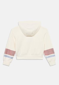 Κοντή μπλούζα με κουκούλα σε κρεμ ύφασμα, διαθέτει κουκούλα, κόκκινες και μπλε διακοσμητικές λεπτομέρειες στα μανίκια και εφαρμοστό λάστιχο στη μέση.