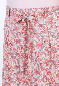 Blumiger Rock aus leichtem Stoff mit einem mehrfarbigen Muster in Rot-, Grün- und Lilatönen. Enthält einen Bindegürtel und Faltenelemente.