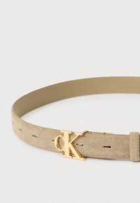 Beigenvärinen mokkanahkavyö, jossa on sileä pinta, kultainen 'CK'-logokolmio ja useita säätöreikiä koon mukauttamiseksi.