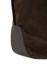 Bruine suède tas met gladde leren accenten. Heeft een afgeronde vorm en contrasterende texturen. Opvallende stiksels omlijnen de leren rand.