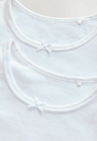 Zwei weiße Baumwoll-T-Shirts mit runden Ausschnitten, dekorativer weißer Stickerei und kleinen Schleifenakzenten am Kragen.