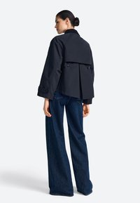 Juoda trumpa striukė su aptemptu dizainu, aukšta apykakle ir sagų detalėmis, derinama su plačiomis džinsinėmis kelnėmis.