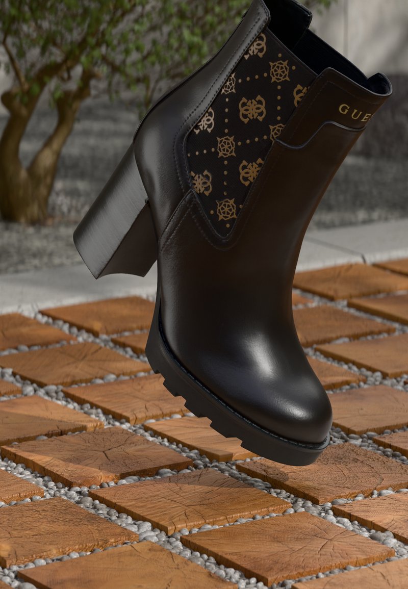 Bottine noire en cuir lisse avec un talon épais, présentant un panneau textile à motif avec des accents dorés. Le sol est en bois texturé et en gravier.