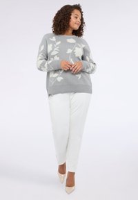 Šedý svetr s květinovým vzorem v bílé barvě, v kombinaci s bílými kalhotami a nahými podpatky. Svetr má kulatý výstřih a ribbované manžety.