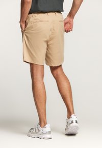Shorts beige con una textura suave, que cuentan con bolsillos laterales y bolsillos traseros de ojal. Combinados con zapatillas deportivas grises y blancas.