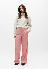 Cremeweißer, strukturierter Pullover kombiniert mit weit geschnittenen, pink gestreiften Hosen. Das Outfit zeichnet sich durch eine lockere Passform und ein Rollkragen-Design aus.