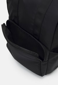Schwarzer Rucksack mit glatter, matter Oberfläche; sichtbare Reißverschlusstasche an der Vorderseite, verstärkte Riemen und robustes, strukturiertes Design.