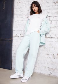 Casaco oversized azul claro sobre uma t-shirt branca com logótipo rosa, combinado com calças azul claro a condizer e ténis brancos com acentos pretos.