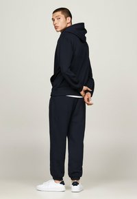 Un hoodie bleu marine avec une coupe décontractée et une poche kangourou, associé à un pantalon de jogging assorti. Des baskets blanches avec des accents bleu marine complètent le look.