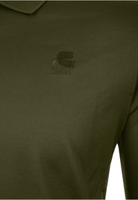 Dunkelgrünes Poloshirt mit einem strukturierten, gestickten Logo eines bärtigen Männerprofils auf der Brust.