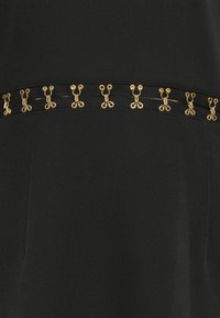 Black garment featuring a flat design with a distinctive gold decorative band detailing a pattern of loops. Smooth texture, fitted silhouette.