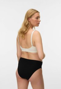 Grudnjak boje kreme s podesivim naramenicama i zatvaranjem na leđima, uparen s crnim gaćicama visokog struka od glatkog materijala.