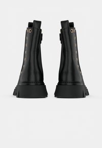 Botas negras hasta el tobillo con un acabado de cuero suave, ojales dorados, lengüetas de tracción planas y una suela de goma negra gruesa con un borde dentado.