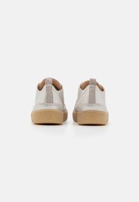 Chaussures beige clair en cuir texturé, avec une doublure en cuir souple couleur tan et une semelle en caoutchouc marron. Conçues avec une boucle au talon pour un enfilage facile.