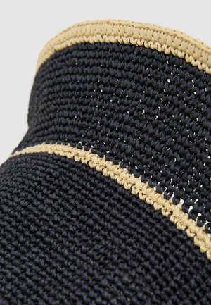 Prim-plan cu o pălărie neagră din paie țesute, cu o margine împletită bej de-a lungul borului și a benzii coroanei.